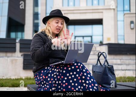 Young woman speaks sign language on a video call on a laptop outdoors. The deaf-mute girl communicates with gestures Stock Photo