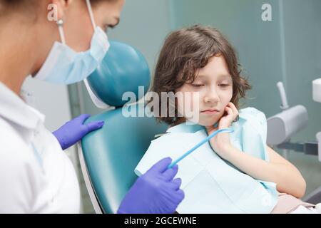 Adorable little boy having toothache, sitting in dental chair at clinic Stock Photo