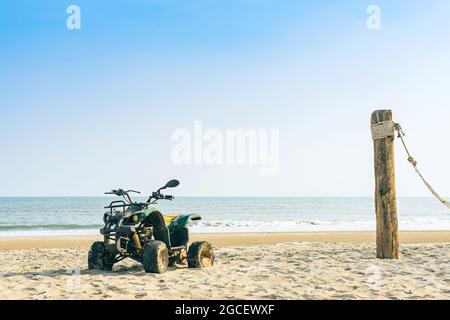 Vintage green ATV on the sandy beach. Quad ATV all terrain vehicle parked on beach, Motor bikes ready for action with summer sun flaring on bright day Stock Photo