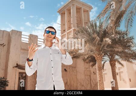 Happy man gestures and smiles while talking on the phone against the backdrop of a wind tower in the old Bur Dubai Creek neighborhood Stock Photo