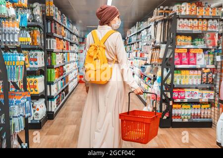 23 February 2021, Dubai, UAE: woman in a Muslim headscarf and a medical face mask in the household chemicals department selects the desired product Stock Photo