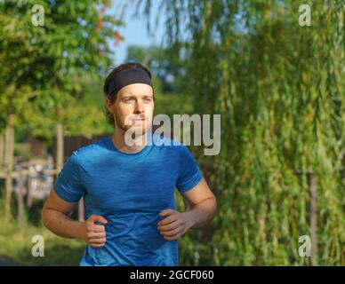 Athletic european man in sportswear jogging on road in green park on beautiful summer day Stock Photo