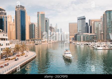 The boat sails along the canal in the Dubai Marina area against the backdrop of numerous residential skyscrapers and hotels Stock Photo