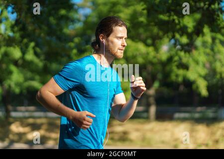 Young handsome active sportsman in blue shirt running on hot sunny day in nature Stock Photo
