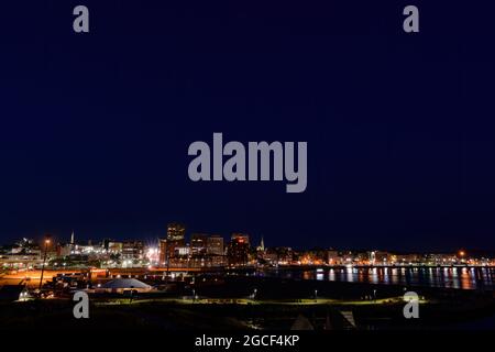 Saint John, NB, Canada - August 1, 2021: Looking east at the skyline of Saint John at night. Light from the city reflected in harbor. Dark blue sky. Stock Photo