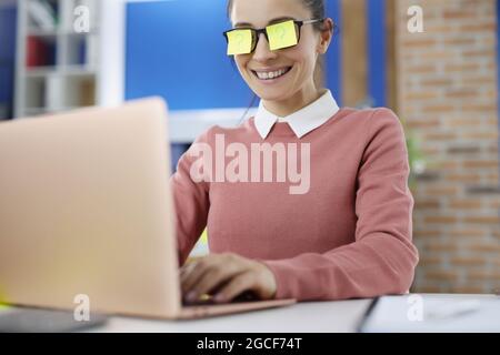 Young smiling woman with yellow stickars on glasses with question mark works on laptop Stock Photo