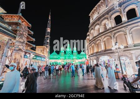 26 February 2021, UAE, Dubai: Visitors and tourists walk through the streets of the Global Village illuminated in the evening with pavilions of many c Stock Photo