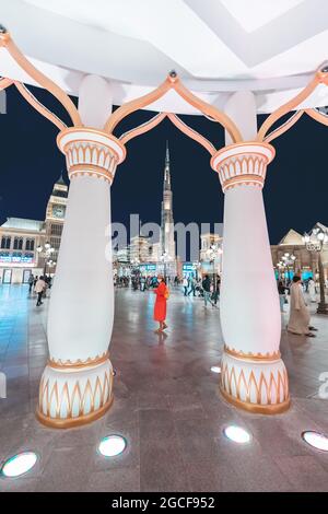 26 February 2021, UAE, Dubai: Visitors and tourists walk through the streets of the Global Village illuminated in the evening with pavilions of many c Stock Photo