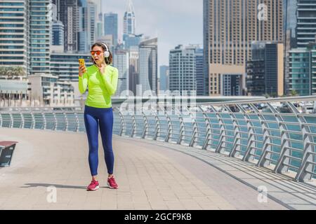 Tired woman runs along the Dubai Marina embankment and checks her pulse by putting her finger to her neck. Health and safety of the human cardiovascul Stock Photo