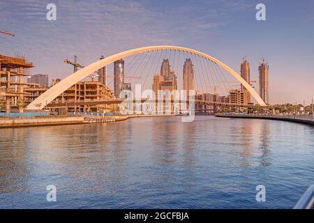 Tolerance bridge and promenade embankment along Dubai Creek Canal with large construction site Stock Photo