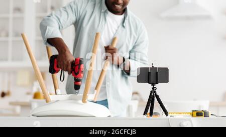Handyman blogger shooting video instructions for assembling furniture at home with own hands, using electric drill, crop. Man making chair, screwing d Stock Photo
