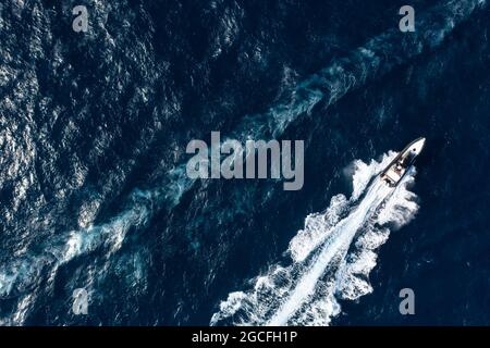View from above, stunning aerial view of a boat cruising on a blue water creating a wake. Costa Smeralda, Sardinia, Italy. Stock Photo
