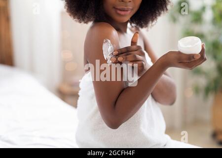 Unrecognizable black lady applying body cream on shoulder after shower in morning at home. Cropped view of African American woman making beauty proced Stock Photo