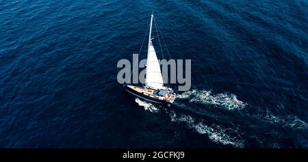 View from above, stunning aerial view of a sailboat sailing on a blue water at sunset. Costa Smeralda, Sardinia, Italy. Stock Photo