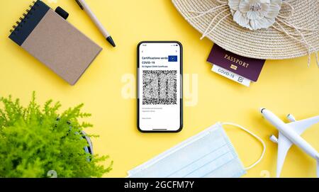 An aircraft model, sun hat, face mask, passport and a smartphone with the Green Pass, are arranged on a yellow background. Stock Photo