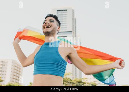 young Hispanic gay man wearing multicolored flag in the street feeling happiness Stock Photo