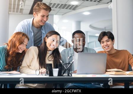 Collaboration Concept. Portrait of smiling multiethnic people sitting at table in modern workspace using laptop, watching tutorial or webinar, happy m Stock Photo