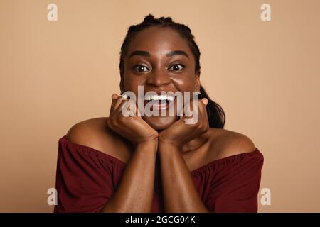 Closeup portrait of young emotional black woman in love posing over beige studio background, having romantic mood, smiling at camera. Millennials phot Stock Photo