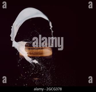 A cup of coffee in a glass with milk splashes on black background Stock Photo