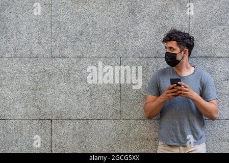 Young latin man with face mask using phone Stock Photo