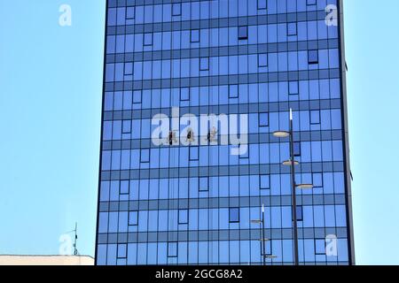 Nis, Serbia - August 08, 2021 Three window washers on a large building using a rope and cleaning windows on a sunny summer day in the city of Nis Stock Photo