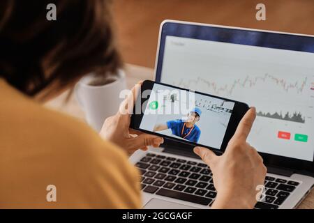 Woman watching delivery man on security camera cctv video on mobile phone while working at home office - Focus on smartphone Stock Photo