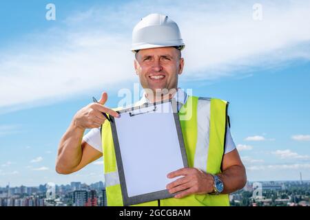 Builder in white hardhat holds clipboard and pointing finger to paper sheet Stock Photo
