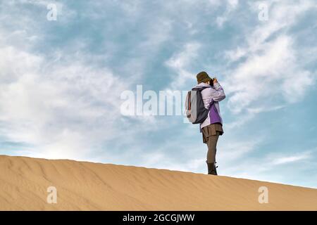 asian woman photographer standing on top of a sand dune taking a picture Stock Photo