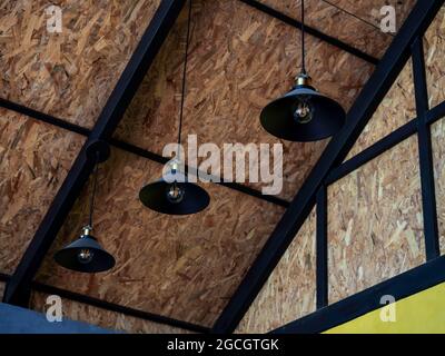 Three black retro style round hanging ceiling lights decoration under the wooden roof construction. Stock Photo