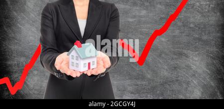 Real estate housing market bubble inflation. Realtor holding miniature house with red chart going up in blackboard background. Panoramic banner Stock Photo