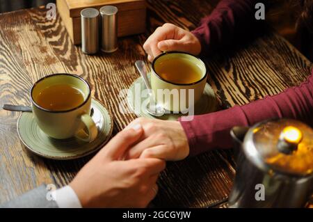 Close up of young couple holding hands in a cafe and drinking tea. Romantic time Stock Photo