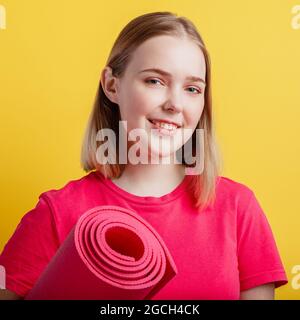 Woman Portrait with yoga mat on color background. Healthy young blonde lady in pink sport outfit smiling while standing with mat for yoga or sport Stock Photo