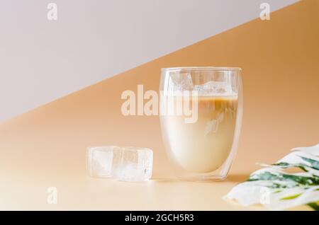 Iced cube in a glass that cover with vapour of latte coffee with monstera leaf and iced cube on the floor. Summer drink concept. Stock Photo