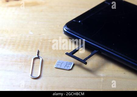 Sim CARD Ejector and Smartphone at Wooden Table Stock Photo