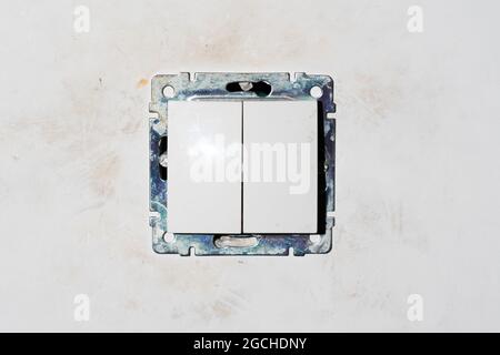 two dirty light switch plastic buttons without front frame on dirty white gray beige raw rough wall. no people. unrepaired electricity control panel Stock Photo