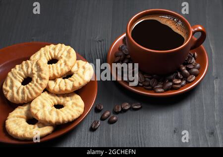 Cup of coffee and cookies with desiccated coconuts in brown dishware on black wooden table Stock Photo