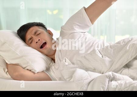Young asian man yawning and stretching while waking up in the morning Stock Photo