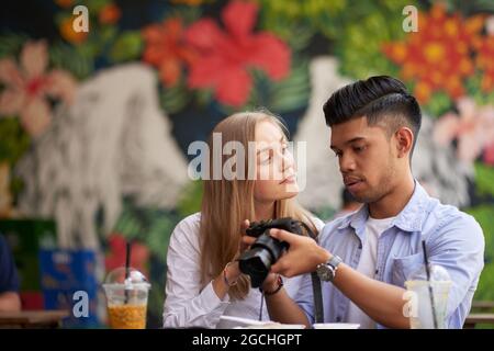 Diverse couple looking at photos they made on digital camera during short trip to nearby town Stock Photo