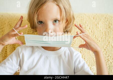 Portrait of a little girl putting on a medical protective mask. Coronavirus protection concept, quarantine Stock Photo