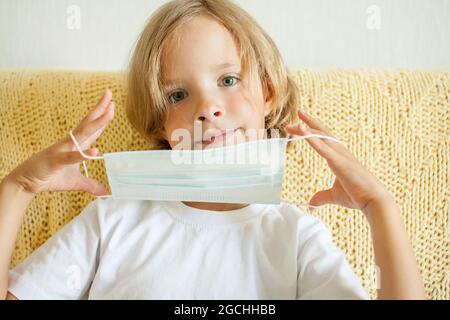 Portrait of a little girl putting on a medical protective mask. Coronavirus protection concept, quarantine Stock Photo