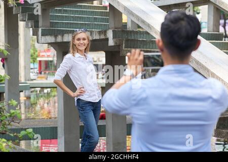 Beautiful attractive young woman posing for photo in front of boyfriend with smartphone Stock Photo