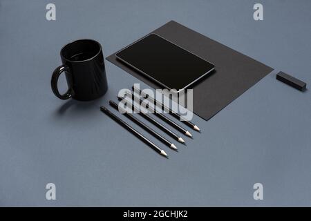 Flat lay of blank black paper sheet, black stationery items and coffee cup on gray desktop. Mock up Stock Photo