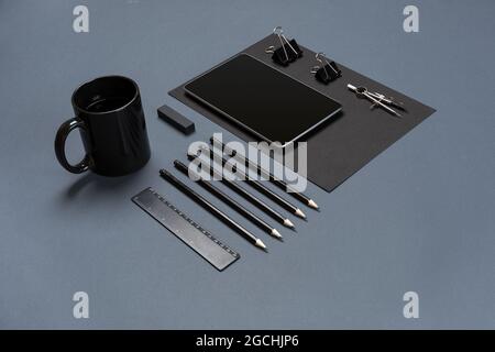 Flat lay of blank black paper sheet, black stationery items and coffee cup on gray desktop. Mock up Stock Photo