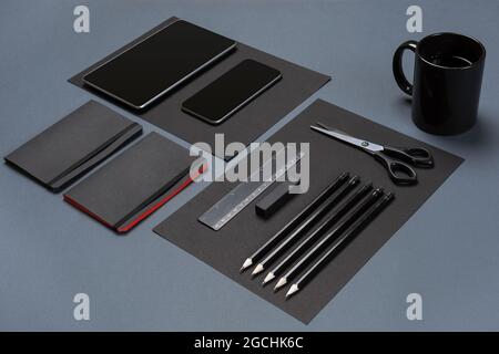 Flat lay of blank black paper sheet, black stationery items and coffee cup on gray desktop. Mock up Stock Photo