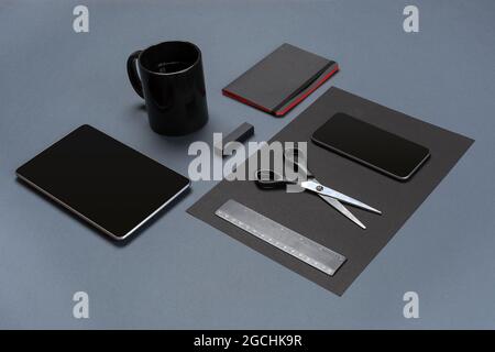 Flat lay of blank black paper sheet, black stationery items and coffee cup on gray desktop. Mock up Stock Photo