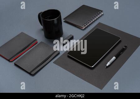 Flat lay of blank black paper sheet, black stationery items and coffee cup on gray desktop. Mock up Stock Photo