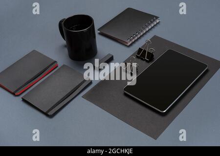 Flat lay of blank black paper sheet, black stationery items and coffee cup on gray desktop. Mock up Stock Photo
