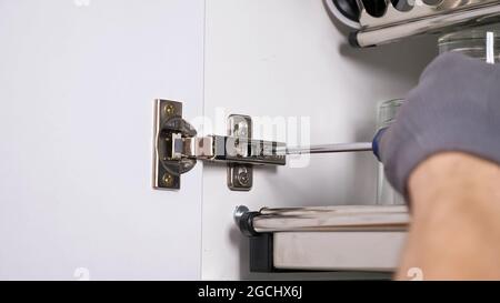 Employee installs door of cabinet twisting screws in hinges Stock Photo