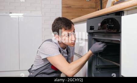 Skilled employee twists screw on broken oven repairing Stock Photo