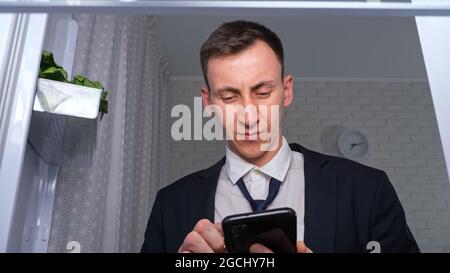 Man loosens tie and makes list to buy food products on phone Stock Photo